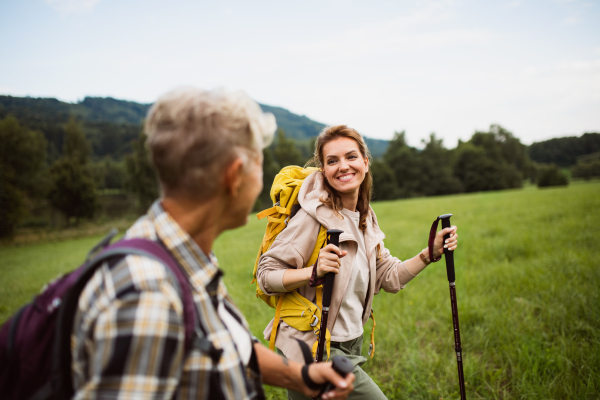 A happy mid adult woman with trekking poles hiking with active senior mother outdoors in nature.