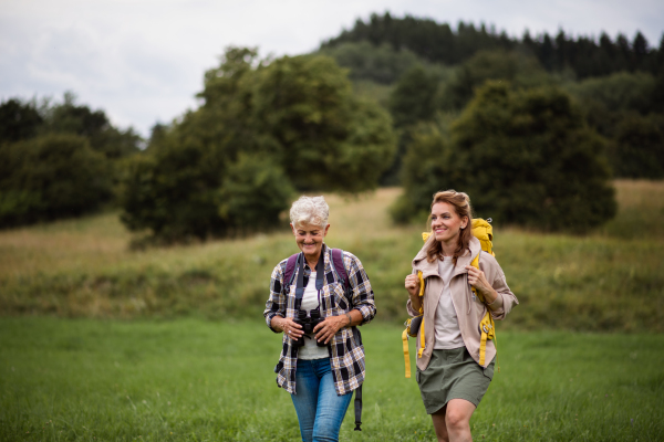 An active senior woman with binoculars hiking with her adult daughter outdoors in nature.