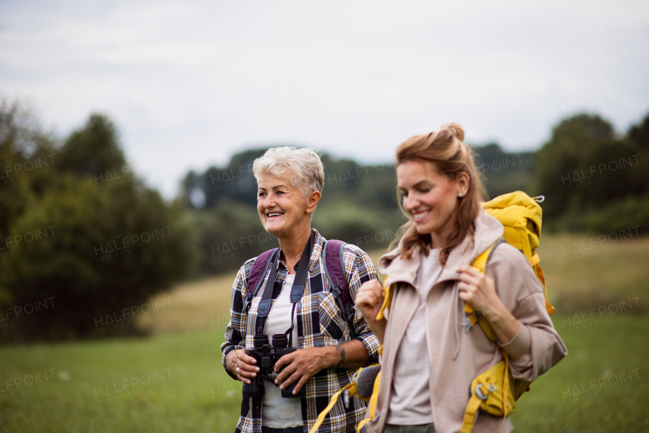 An active senior woman with binoculars hiking with her adult daughter outdoors in nature.