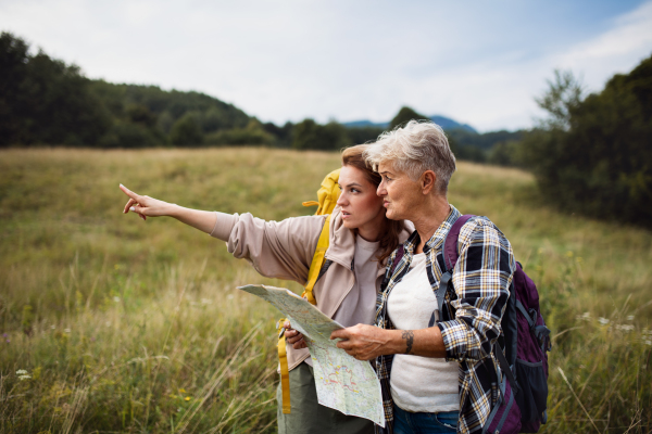 A happy mid adult woman with active senior mother hiking and looking at map outdoors in nature.