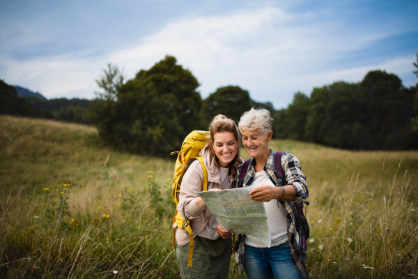 A happy mid adult woman with active senior mother hiking and looking at map outdoors in nature.