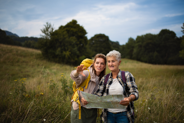 A happy mid adult woman with active senior mother hiking and looking at map outdoors in nature.