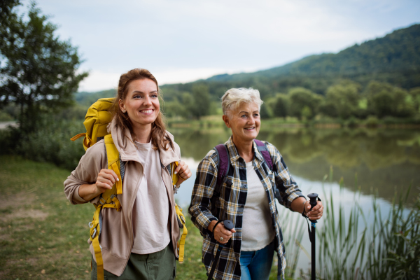 A happy senior woman with trekking poles hiking with adult daughter outdoors in nature.