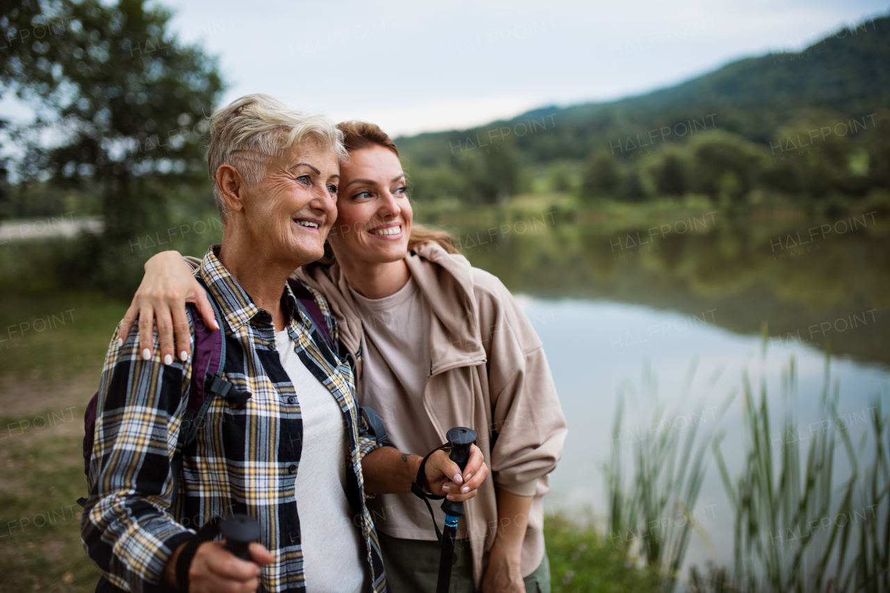 A happy senior mother hiker embracing with adult daughter when looking at lake outdoors in nature