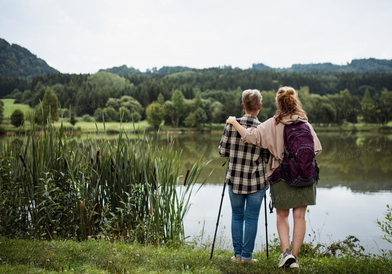 A rear view of senior mother embracing with adult daughter when standing by lake outdoors in nature