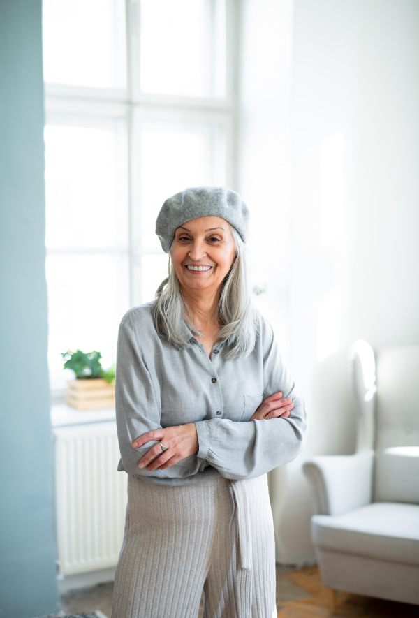 Studio portrait of senior woman with gray beret standing indoors at home.