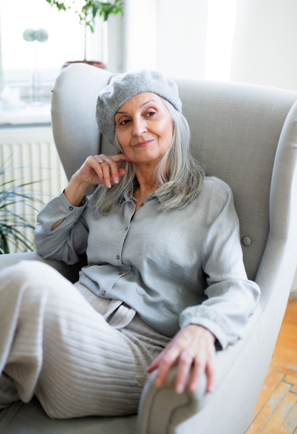 Studio portrait of senior woman with gray beret sitting indoors against dark background.