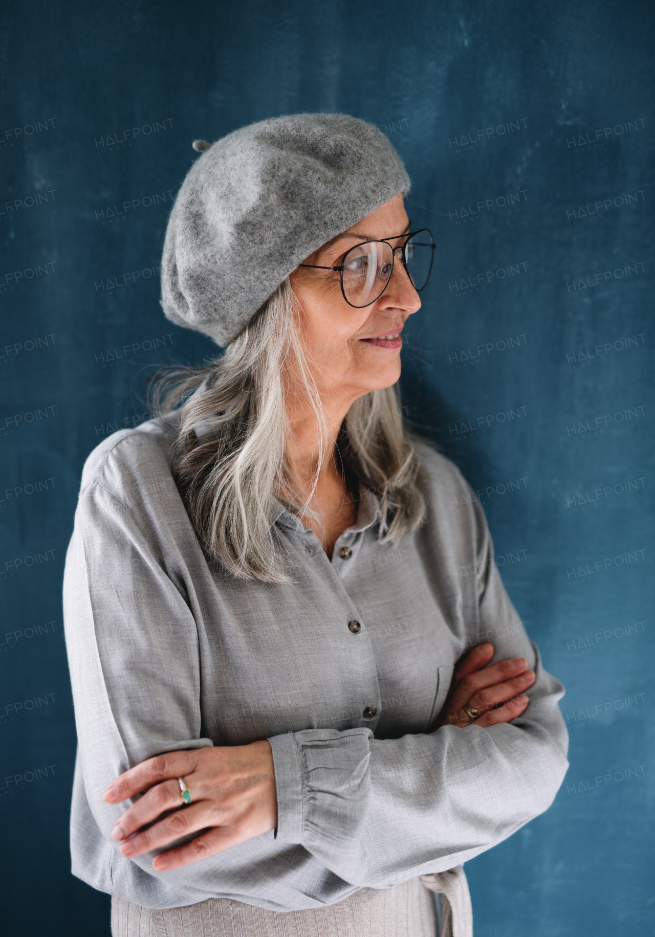 Studio portrait of senior woman with gray beret standing indoors against dark background.