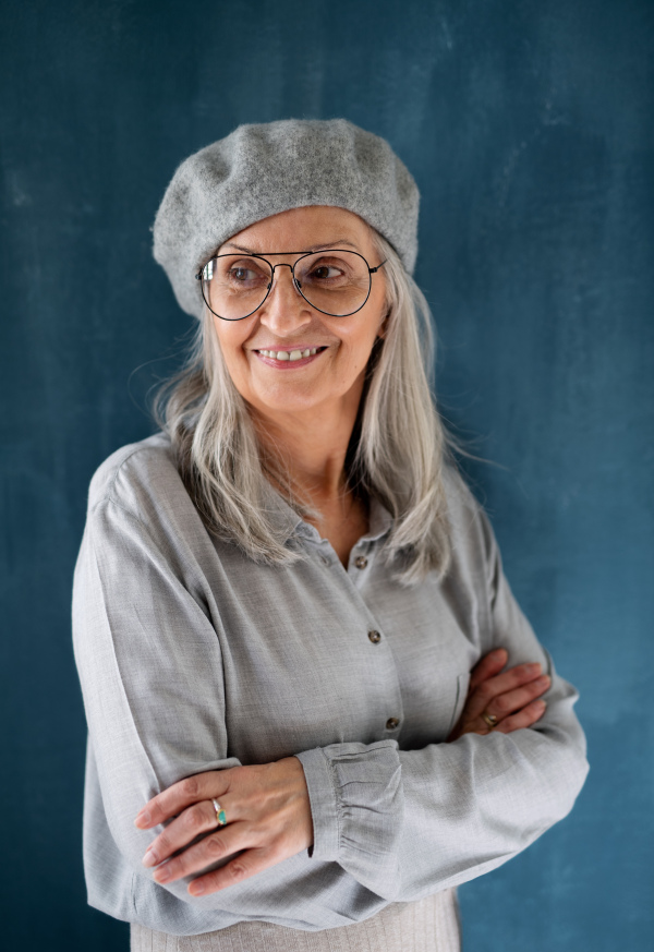 Studio portrait of senior woman with gray beret standing indoors against dark background.