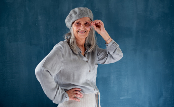 Studio portrait of senior woman with gray beret standing indoors against dark background.