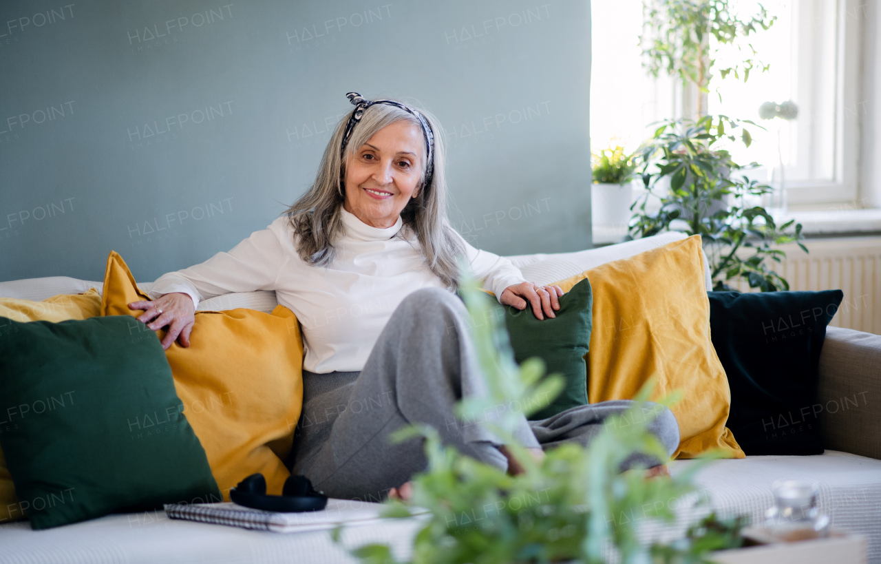 Portrait of senior woman sitting indoors on sofa at home, relaxing and looking at camera.