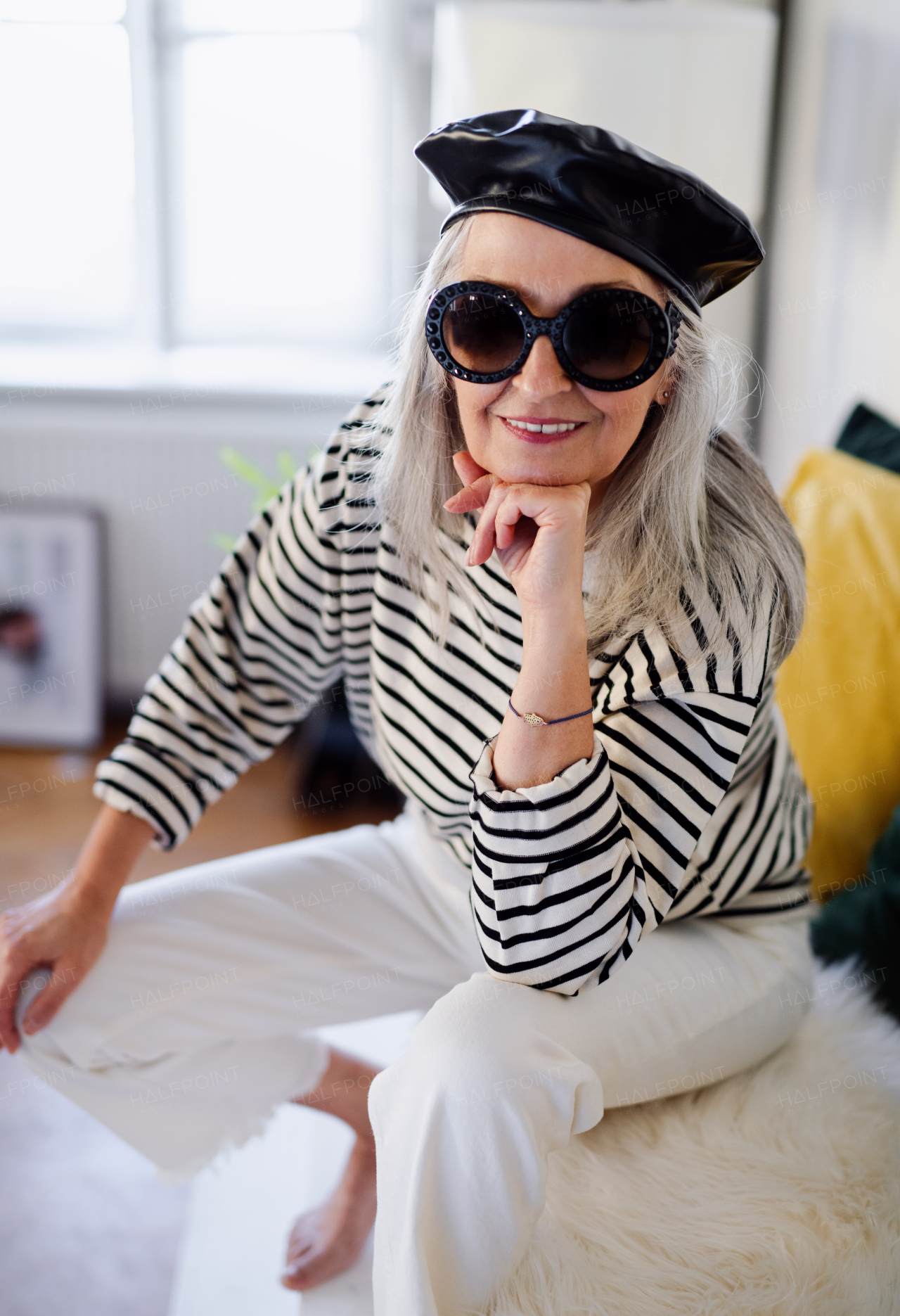 Studio portrait of senior woman with sunglasses and beret standing indoors against dark background.