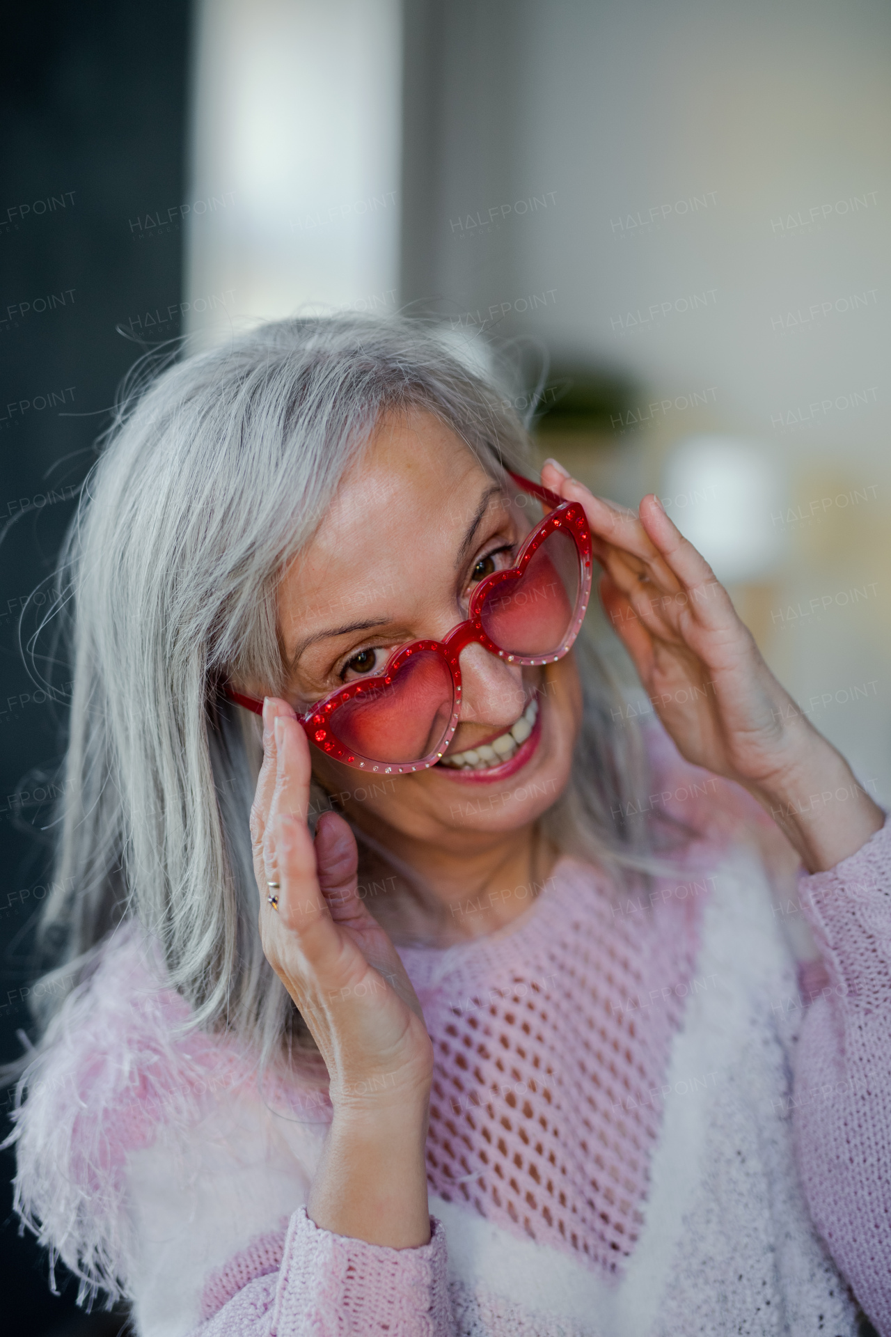 Portrait of cheerful senior woman with sunglasses and headphones indoors at home, laughing.