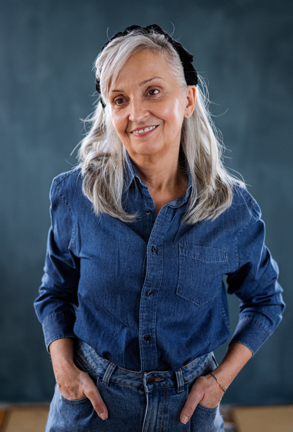 Front view portrait of senior woman standing indoors against dark background, standing.