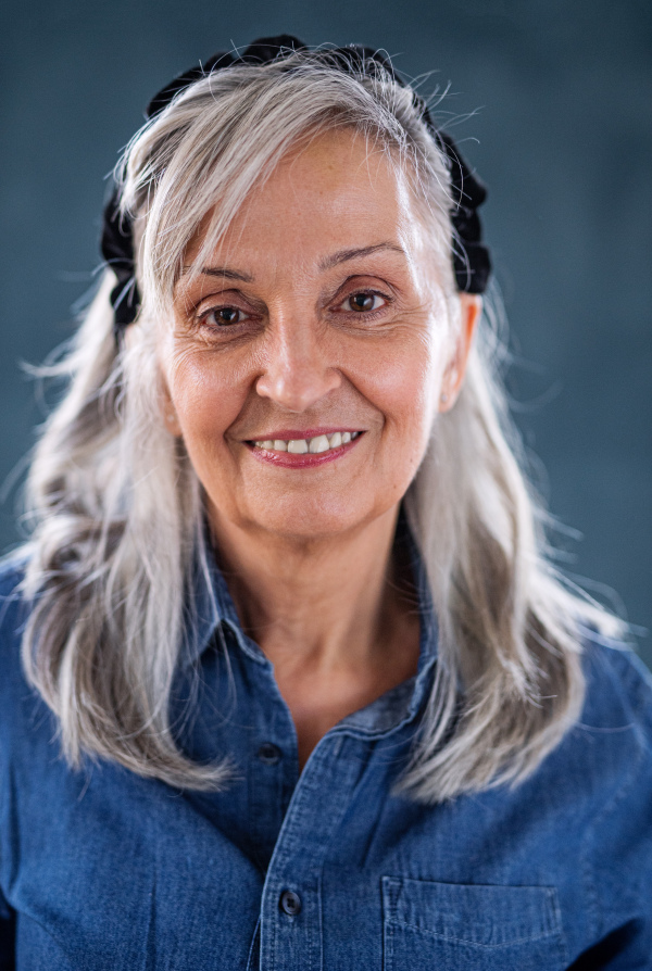 Front view portrait of senior woman standing indoors against dark background, looking at camera.