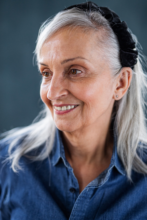 Front view portrait of senior woman standing indoors against dark background.