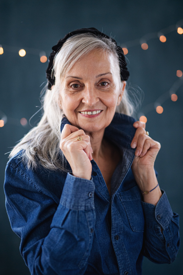 Front view portrait of senior woman standing indoors against dark background, looking at camera.