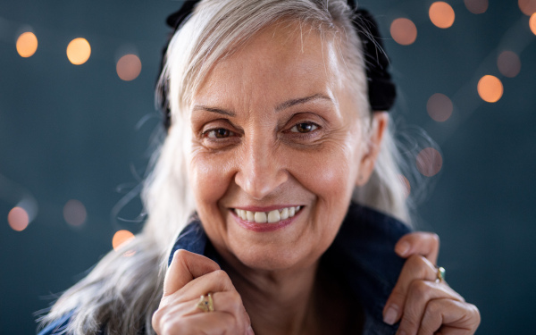 Front view portrait of senior woman standing indoors against dark background, looking at camera.