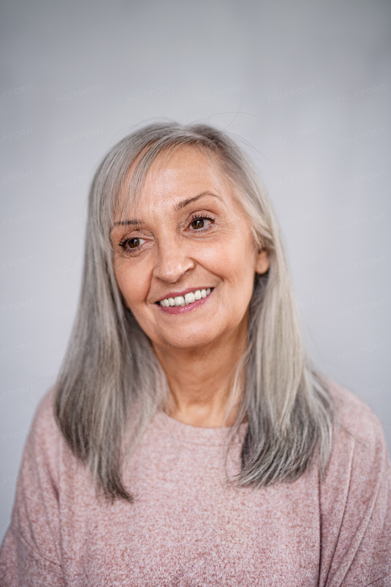 A front view portrait of happy senior woman standing indoors at home.