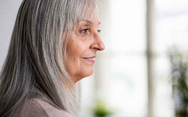 Side view close-up portrait of senior woman standing indoors at home. Copy space.