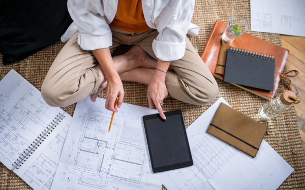 Top view of unrecognizable senior woman architect sitting on floor indoors at home, working.