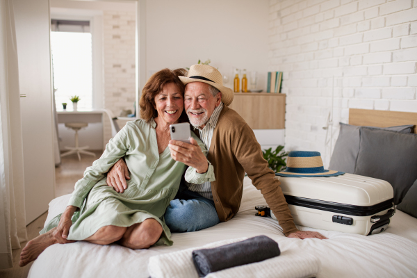 Portrait of happy senior couple with smartphone in hotel room, taking selfie.