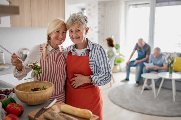 Group of cheerful senior friends having party indoors, cooking and looking at camera.