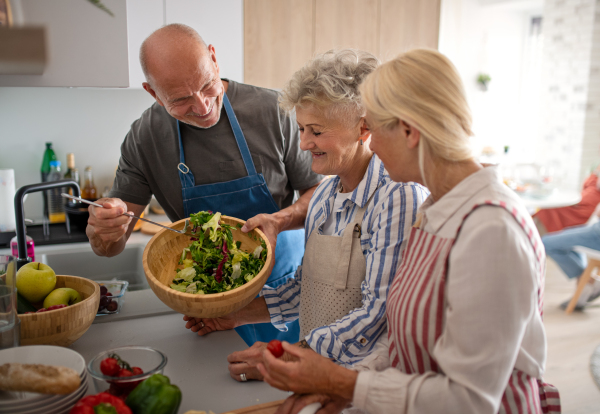 Group of cheerful senior friends having party indoors, cooking and talking.