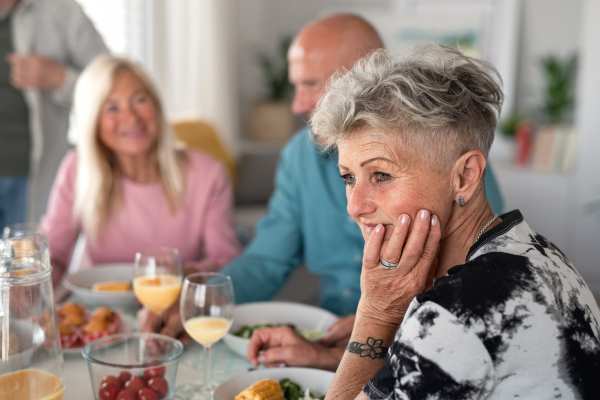 A sad senior woman with friends having party indoors, eating at the table.