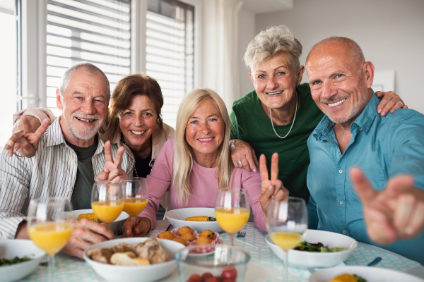 Group of cheerful senior friends having party indoors, looking at camera when eating.