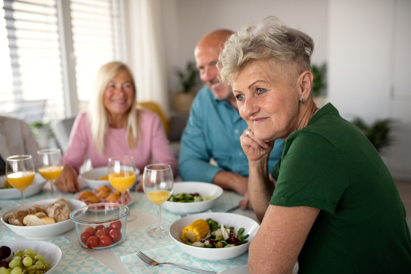 A senior woman with friends having party indoors, eating at the table.