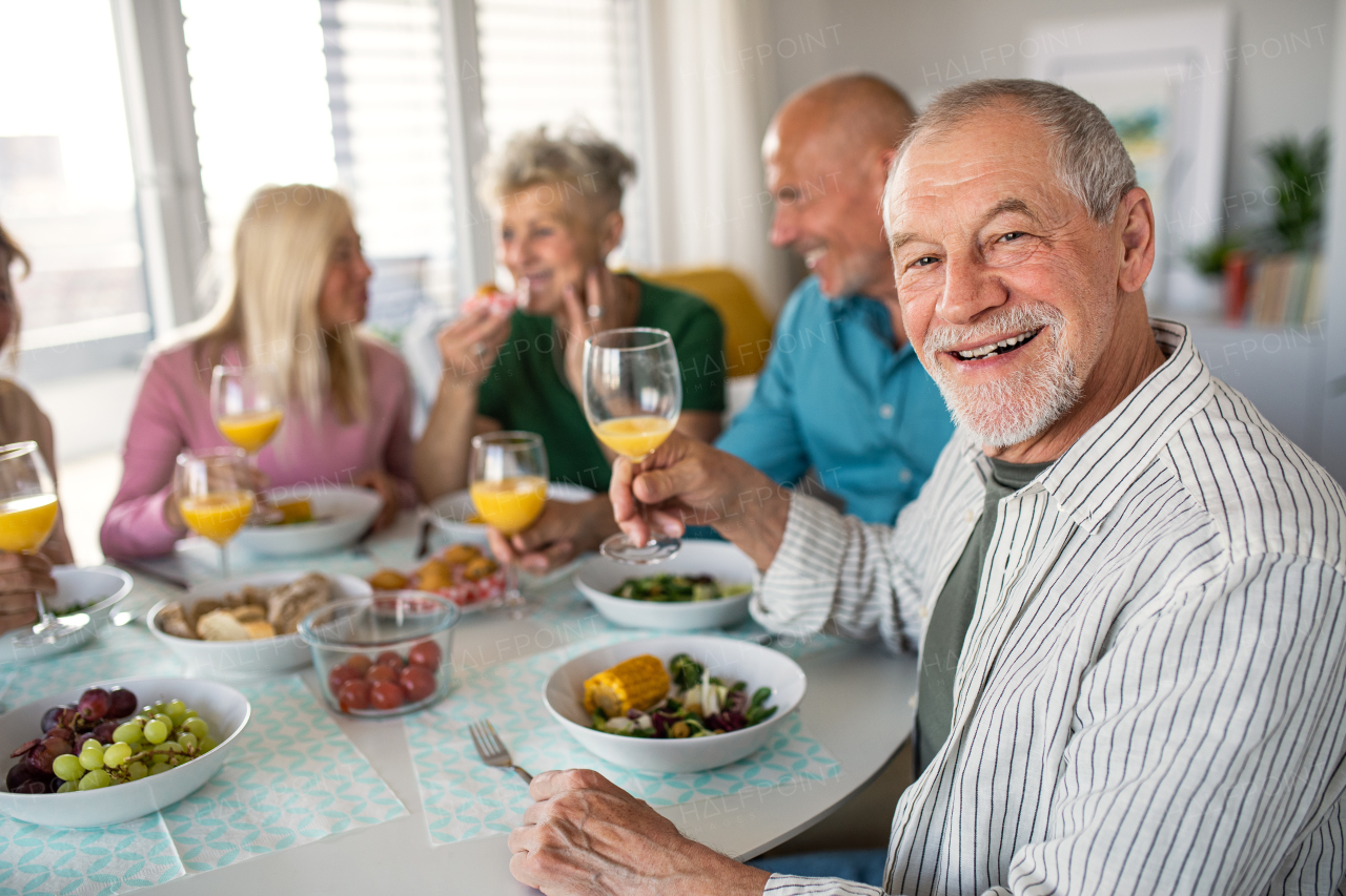 A senior man with friends having party indoors, eating at the table.