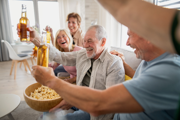 A group of cheerful senior friends watching movie indoors, party, social gathering and having fun concept.