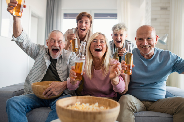 Group of cheerful senior friends watching movie indoors, party, social gathering and having fun concept.