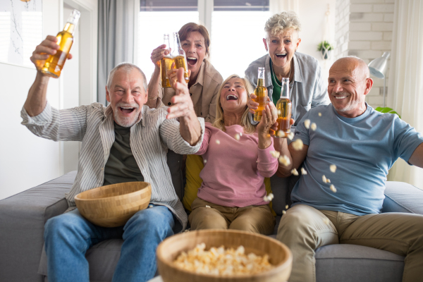 Group of cheerful senior friends watching movie indoors, party, social gathering and having fun concept.