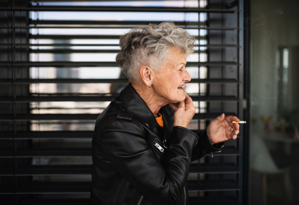 A portrait of senior woman with cigarette standing against black backround, relaxing.