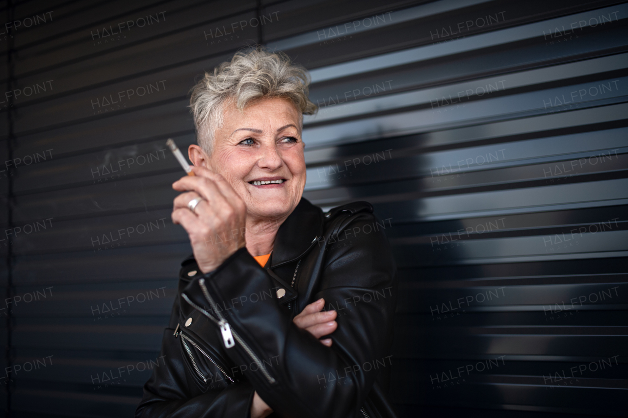 A portrait of senior woman with cigarette standing against black backround, relaxing.