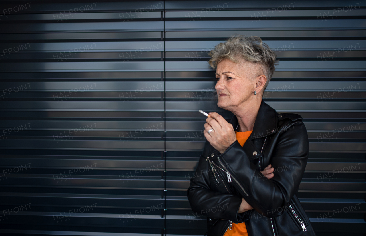 A portrait of senior woman with cigarette standing against black backround, relaxing.