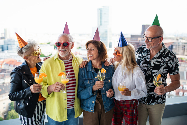 Front view of group of senior friends having party outdoors on balcony, posing for photograph.