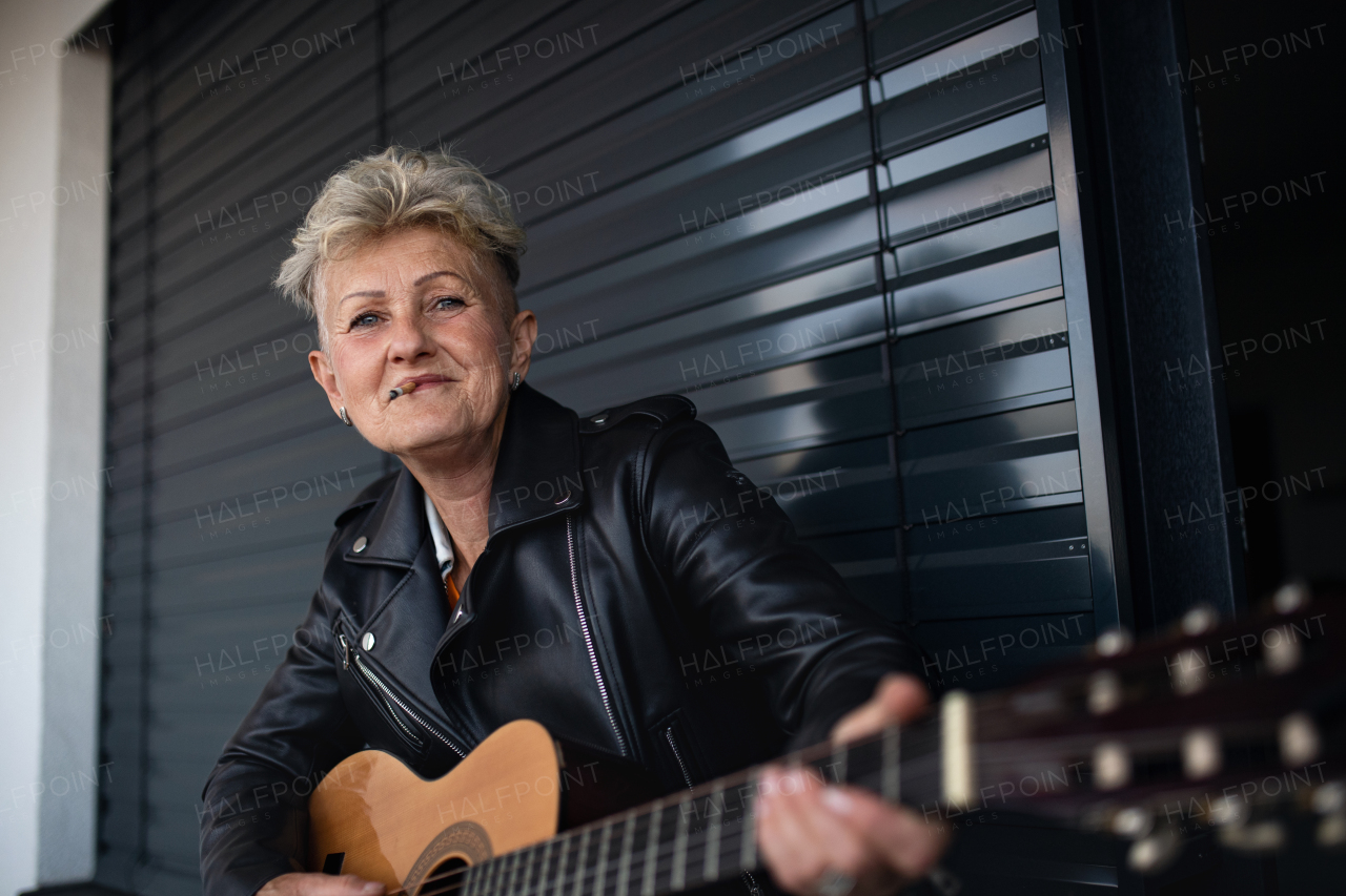 A portrait of senior woman with cigarette standing against black backround, playing guitar.