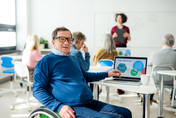 Senior man in wheelchair with teacher attending computer and technology education class.