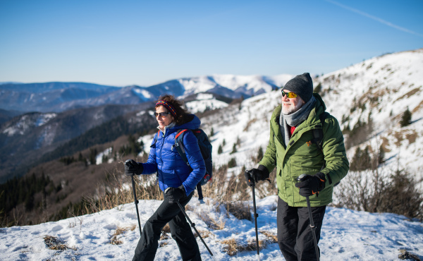 Senior couple with nordic walking poles hiking in snow-covered winter nature, healthy lifestyle concept.