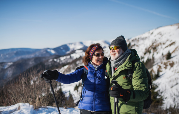 Senior couple hikers with nordic walking poles in snow-covered winter nature, resting.