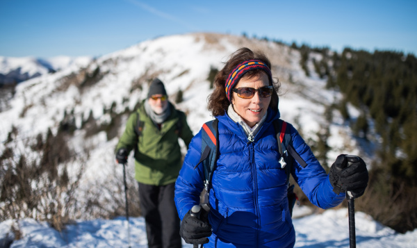 Senior couple with nordic walking poles hiking in snow-covered winter nature, healthy lifestyle concept.