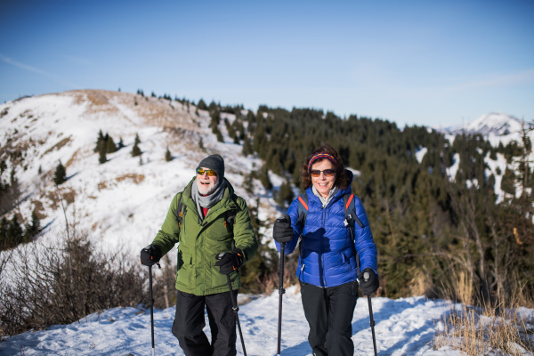 Senior couple with nordic walking poles hiking in snow-covered winter nature, healthy lifestyle concept.