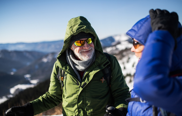 Senior couple hikers resting in snow-covered winter nature, talking.