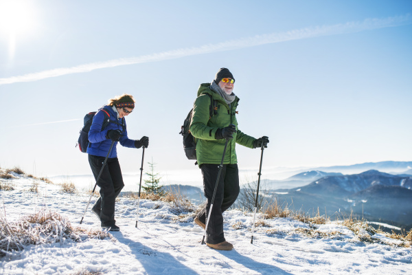 Senior couple with nordic walking poles hiking in snow-covered winter nature, healthy lifestyle concept.