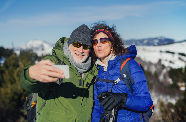 Portrait of senior couple hikers standing in snow-covered winter nature, taking selfie.