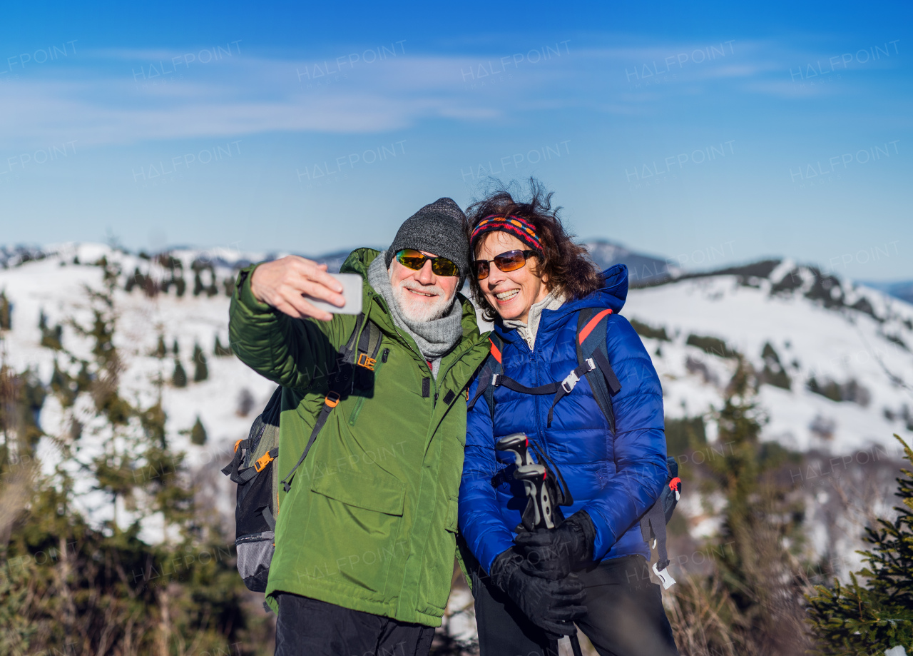 Portrait of senior couple hikers standing in snow-covered winter nature, taking selfie.