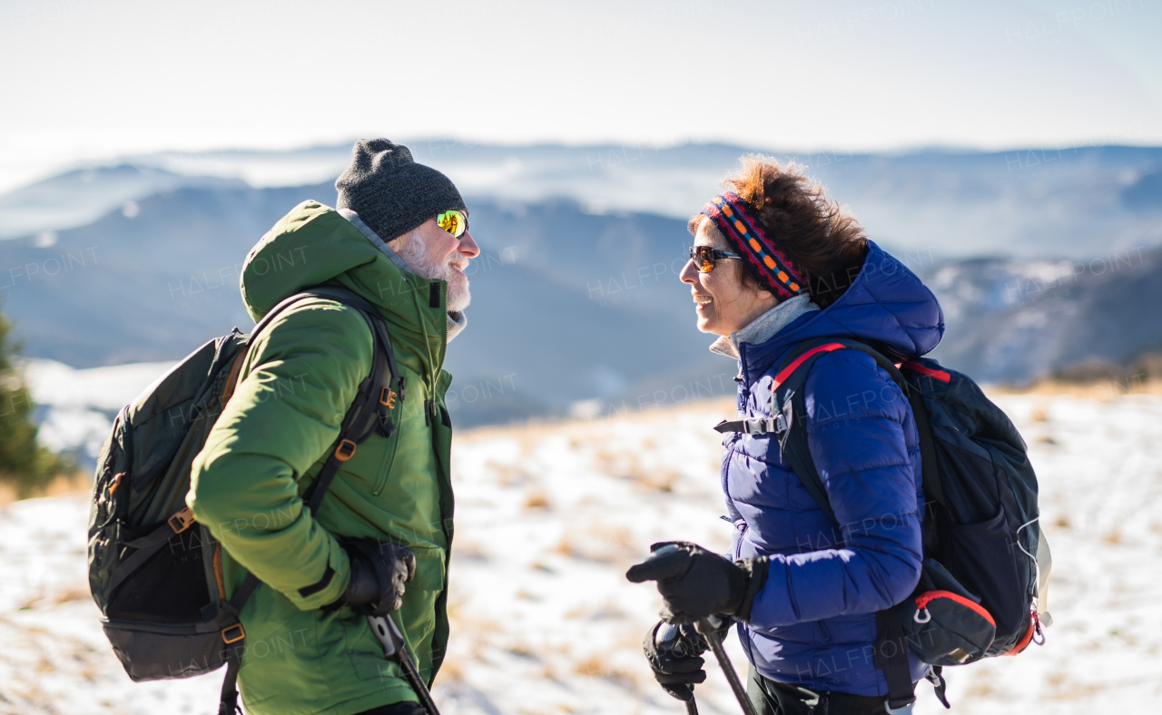 Senior couple hikers resting in snow-covered winter nature, talking.